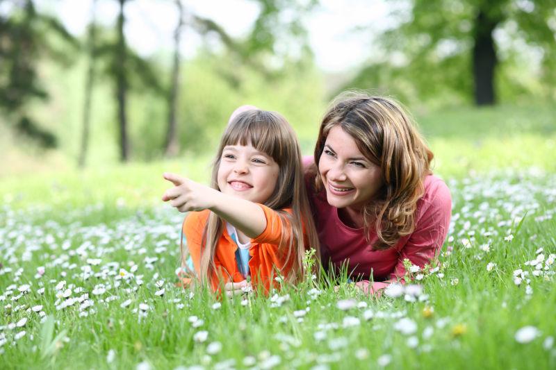 绿色户外背景下开满白色花朵的草地上微笑的母亲和女儿
