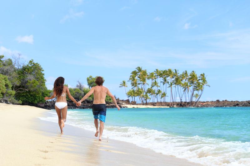快乐的情侣从背后牵着手在热带海滩度假跑步