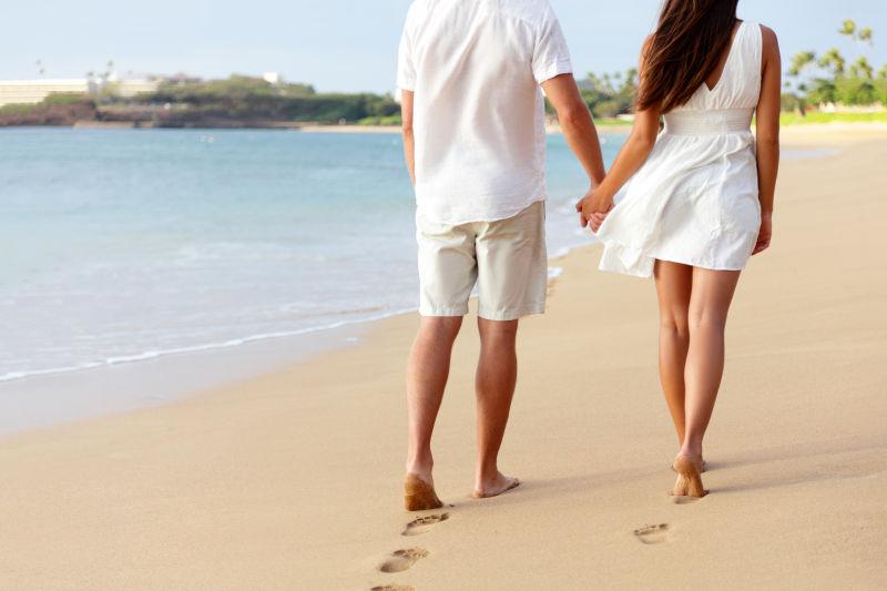 蜜月的赤脚情侣牵着手走在浪漫沙滩度假假期