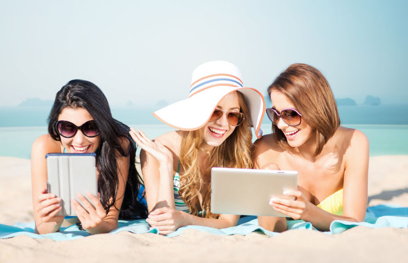 三位美女在沙滩上使用平板电脑