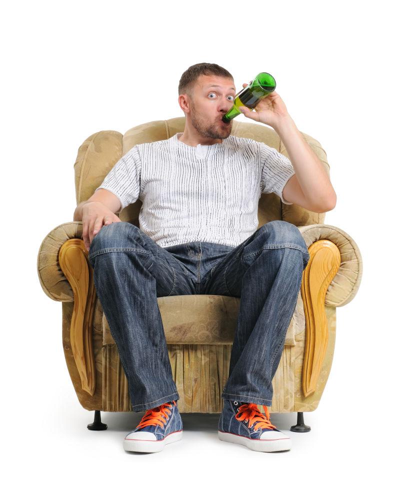白色背景上坐在单人沙发上喝啤酒的男人