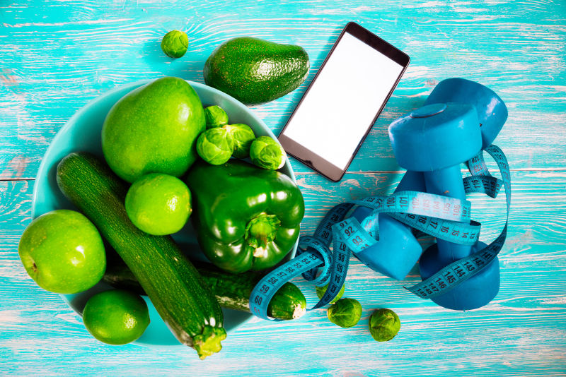 蓝色旧木桌上绿色蔬菜和皮尺手机