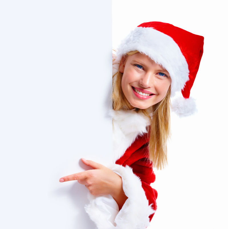 白色背景中藏在空白牌子背后的穿圣诞服装的小女孩