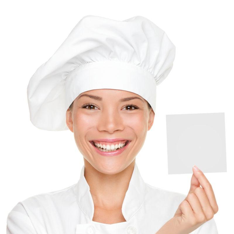 佩戴厨师制服和帽子的美丽的年轻的女厨师出示空白标志牌