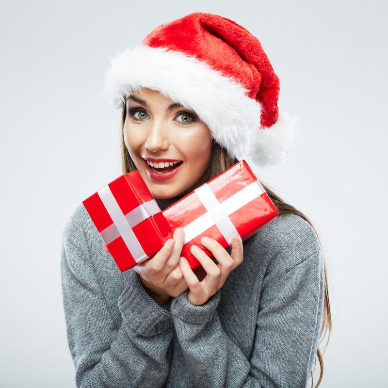 白色背景下戴着圣诞帽子拿着礼物盒子的美女