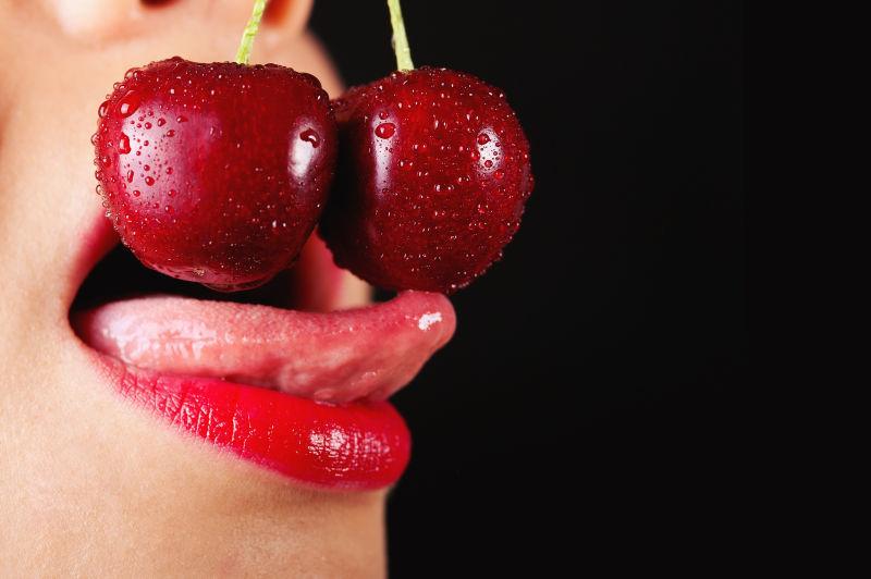 黑色背景下美女把樱桃放在嘴巴前