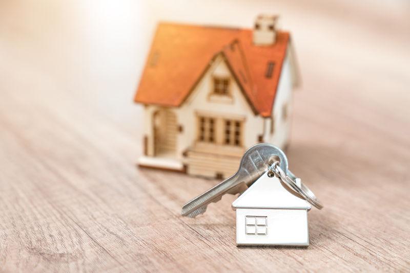 房子钥匙在一个房子形状的钥匙链搁置在木地板上的概念