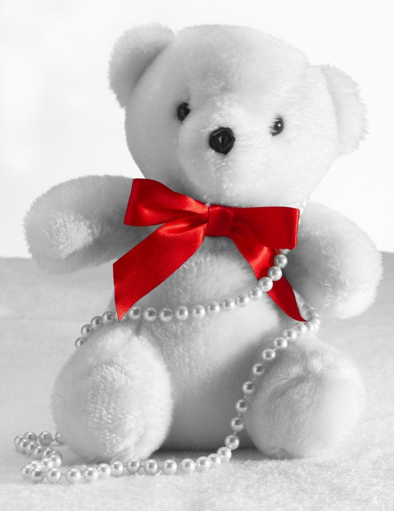 白色背景上一只戴着珍珠和红色蝴蝶结的白色玩具熊