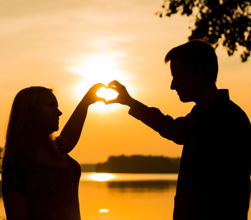 夕阳下湖边用双手做心脏形状的情侣