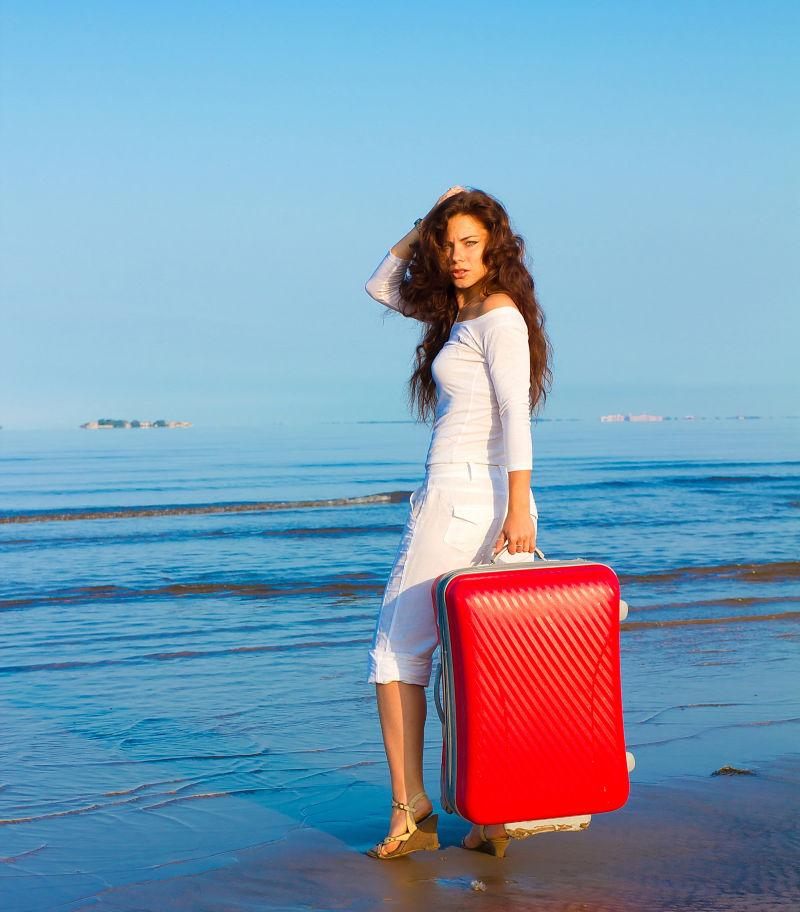 海滩上拿着红色行李的美女