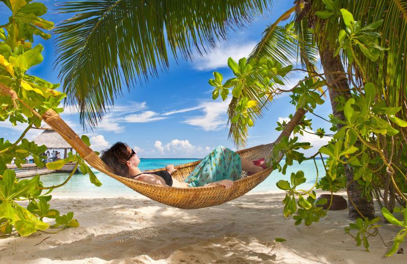 女孩睡在热带马尔代夫海滩棕榈树下的吊床上