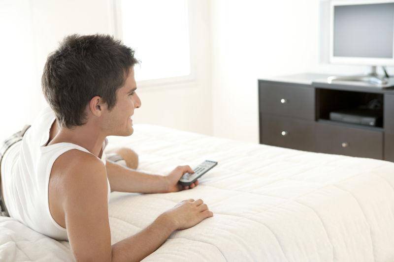 床上拿着遥控器看着电视的男人