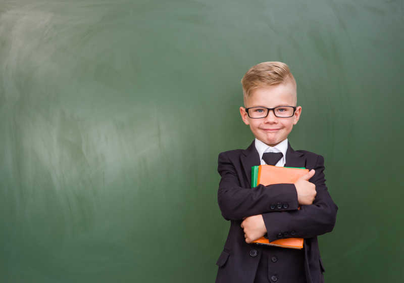 男孩抱着书本站在绿色黑板前