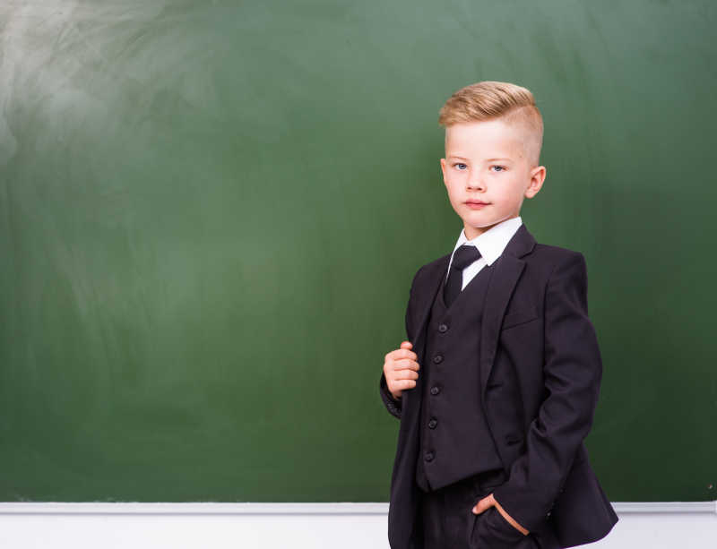 男孩穿着西装站在空荡荡的绿色黑板