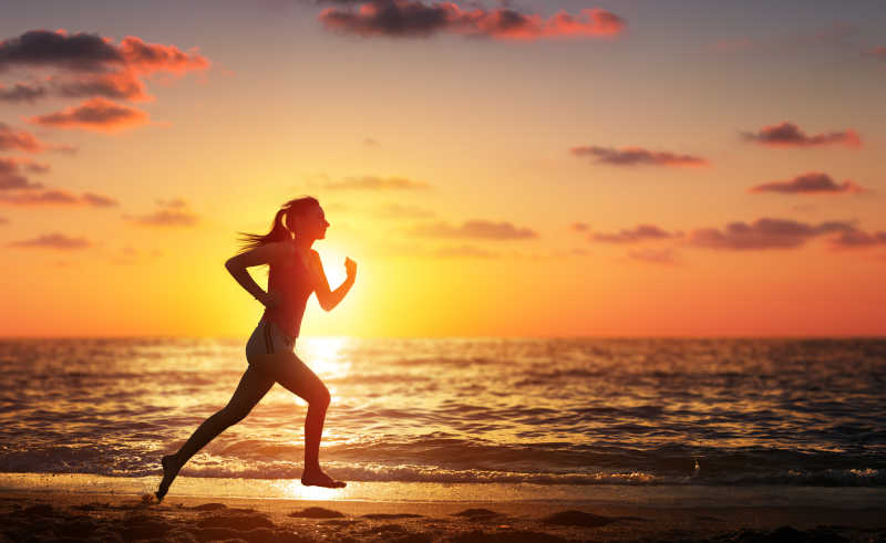 日落时分在海滩奔跑的赛跑女子