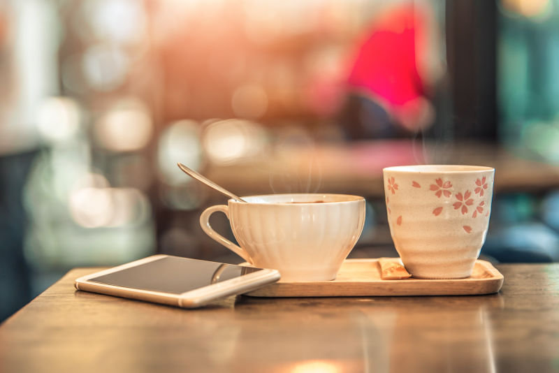 咖啡店木桌上有一个带智能手机的热咖啡杯老式音调