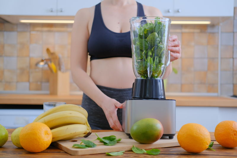 女人把菠菜香蕉和杏仁奶混合在一起制成健康的绿色冰沙