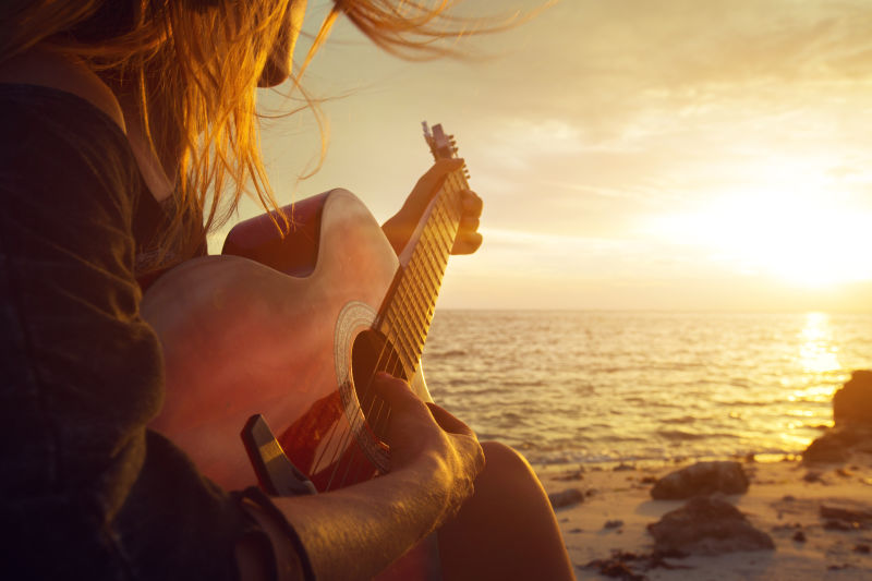 美丽的年轻女子在日落海滩弹吉他
