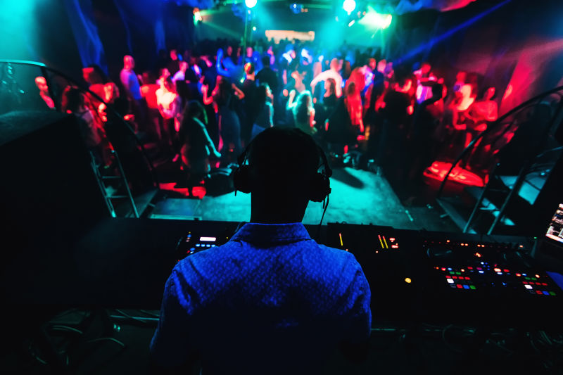 DJ在混音器上演奏音乐的剪影许多人在舞台上的夜总会跳舞