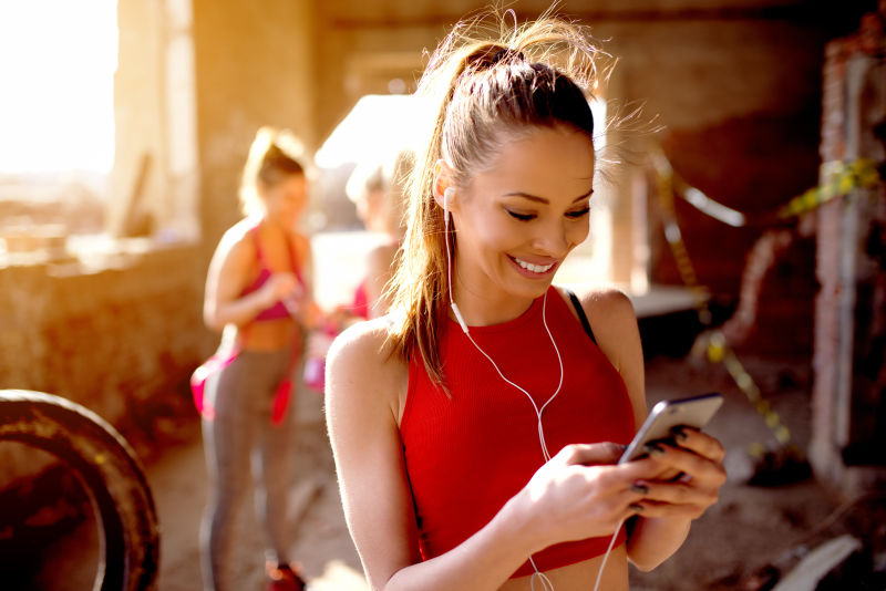 年轻迷人的健身模特在户外锻炼前在智能手机上听音乐燃烧正能量阳光明媚朋友们在后面准备训练