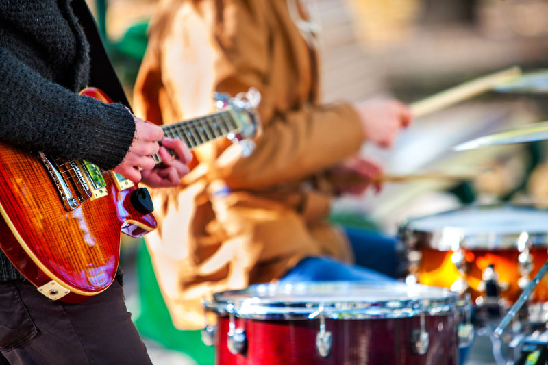 节日音乐乐队在城市公园里用打击乐器演奏带木棍的鼓特写男音乐家身体的一部分锐利是吉他和人的手