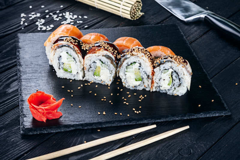 用筷子将寿司卷夹在黑石上-深色背景的寿司特写镜头-传统的日本料理-餐厅-食物菜单-食谱-咖啡馆概念-带复印空间的生活方式