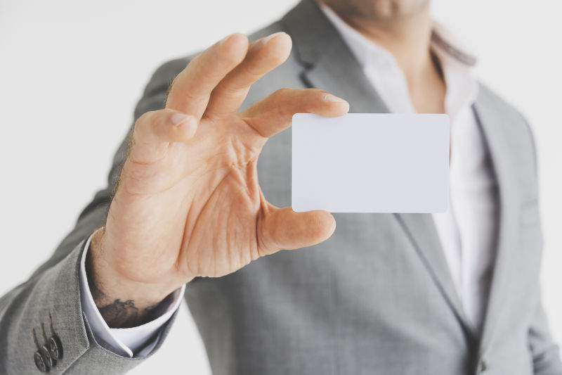 男人拿着白色的名片或空白的白色的信用卡-摆在眼前-塑料银行卡设计在灰色的背景墙上