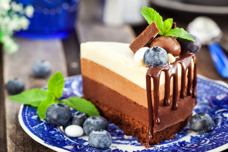 用新鲜蓝莓薄荷和糖果装饰的美味三巧克力慕斯蛋糕