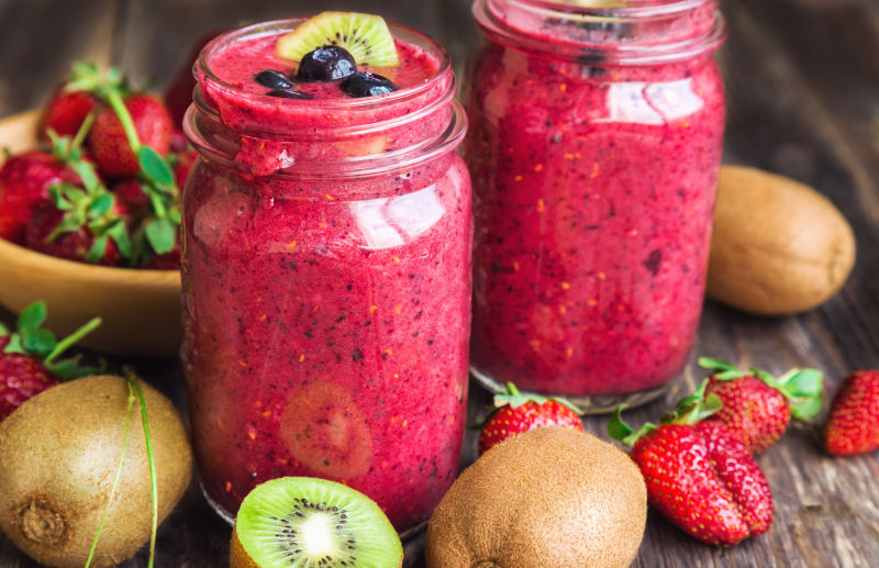 用草莓猕猴桃和蓝莓在乡村木质背景的罐子里冰沙-健康早餐