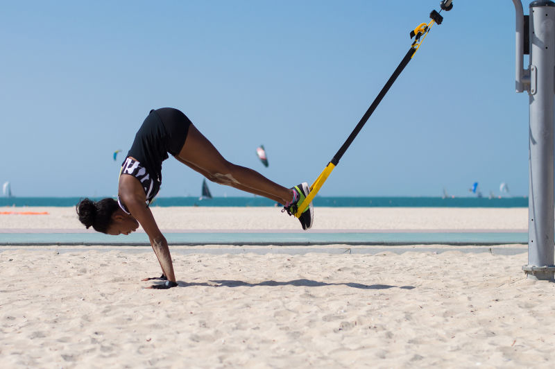 阿拉伯联合酋长国迪拜海滩一名年轻的非洲妇女在用绳索进行悬吊训练时进行了困难的运动