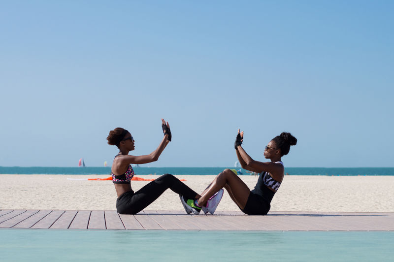 两名非洲裔女性坐在海边一起在阿联酋迪拜海滩锻炼