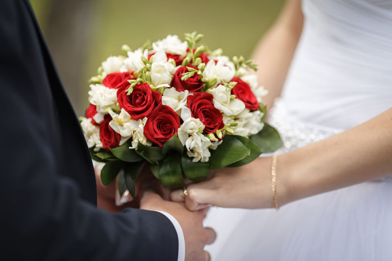 新婚夫妇手上戴着结婚戒指-婚礼花束上戴戒指的新郎新娘之手