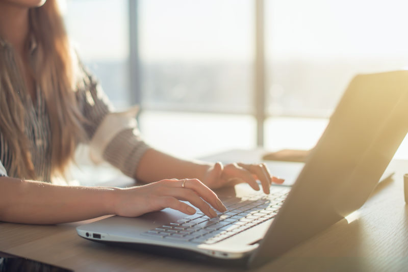 早上女作家在工作场所用笔记本电脑键盘打字女性在网上写博客侧视图特写图片
