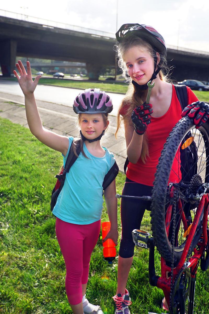骑自行车的女孩举起手来女孩们戴着自行车头盔和自行车用手摇泵女孩给自行车轮胎打气孩子们在桥下修理自行车