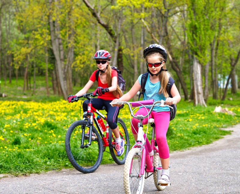 骑自行车的女孩女孩们戴着自行车头盔背着帆布包骑着自行车孩子们争先恐后自行车共享计划节省金钱和时间前景中的孩子是背景中的青少年