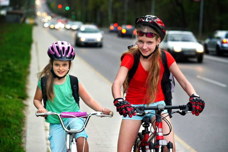 骑自行车的女孩女孩们戴着自行车头盔戴着眼镜背着帆布包骑着自行车女孩们在城市街道的黄色自行车道上骑车路上有汽车