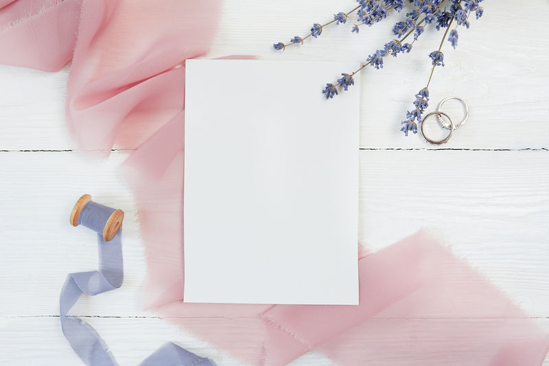 白色空白卡片丝带有两个结婚戒指背景为粉色织物白色背景为薰衣草花用信封和空白卡片模拟平铺俯视图