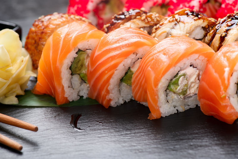 用筷子做寿司-餐馆里的寿司卷日本菜-加利福尼亚寿司卷-配有鲑鱼蔬菜飞鱼卵和鱼子酱特写-日本餐厅菜单