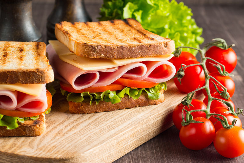 特写的两个三明治与培根-意大利香肠-意大利火腿和新鲜蔬菜在乡村木制砧板-俱乐部三明治概念