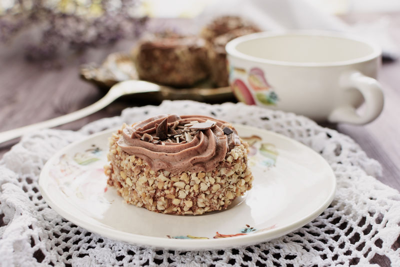 撒有坚果屑的饼干蛋糕-用白陶瓷盘上的巧克力奶油装饰在花边娃娃上