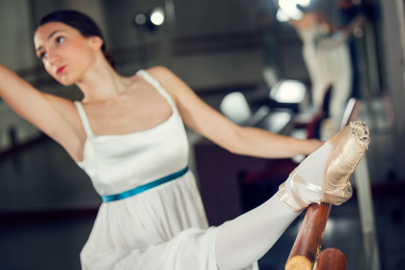 漂亮的古典芭蕾舞演员穿着白色芭蕾短裙一条腿挨着吧台摆姿势