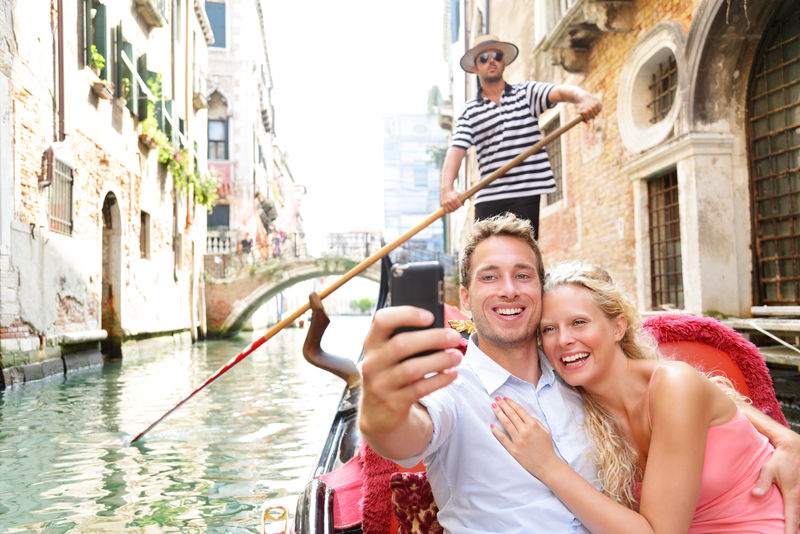 威尼斯的一对夫妇坐着平底船在船上浪漫地度过旅行假期-浪漫的年轻漂亮的夫妇在威尼斯运河的贡多拉自画像航行-意大利