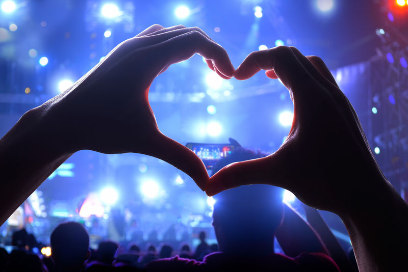 剪影的心形手和现场音乐会的观众群灯光照亮是音乐音乐会的力量
