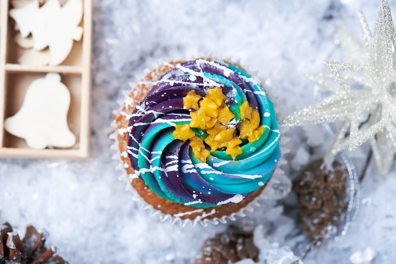 冬季纸杯蛋糕雪上有渐变奶油和金色星星背景是礼物木制玩具圆锥体和雪花冬天的心情俯视图
