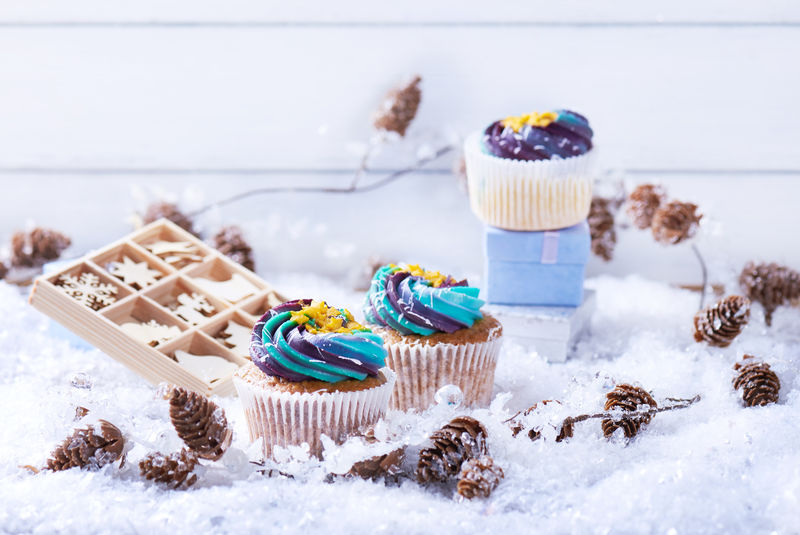 冬季纸杯蛋糕雪上有渐变奶油和金色星星背景是礼物木制玩具圆锥体和雪花冬情