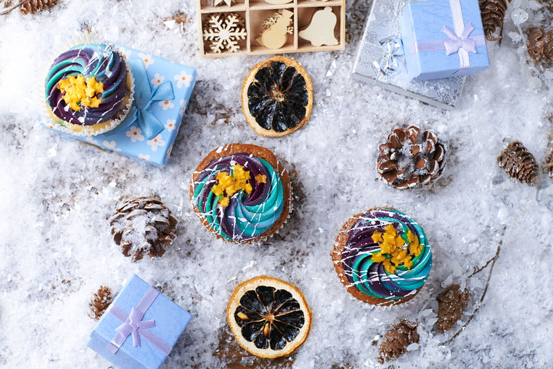 冬季纸杯蛋糕雪上有渐变奶油和金色星星背景是礼物木制玩具圆锥体和雪花冬天的心情俯视图
