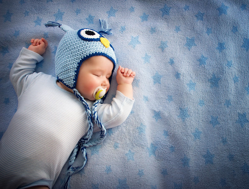 4个月大的戴猫头鹰帽子的婴儿睡在蓝色毯子上
