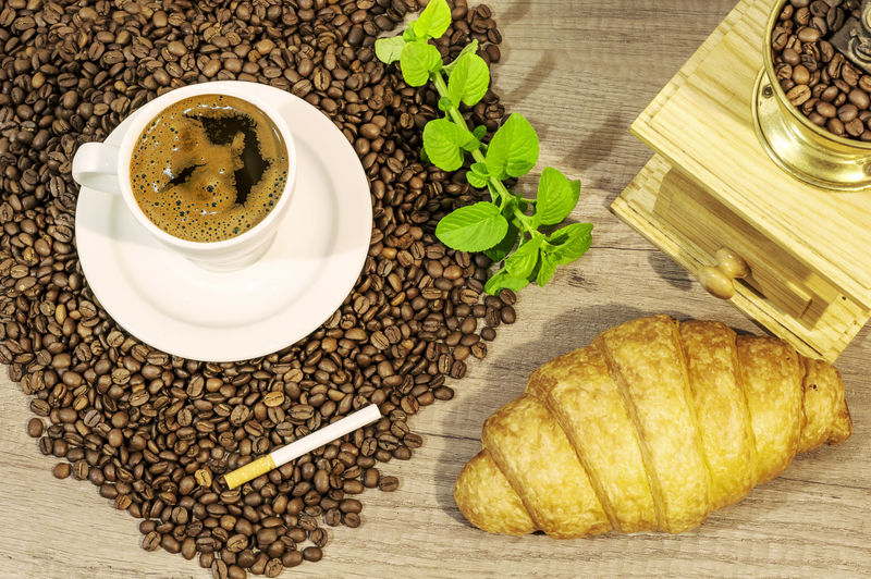 一杯新鲜咖啡咖啡豆牛角面包咖啡研磨机木桌上的雪茄和薄荷茶花