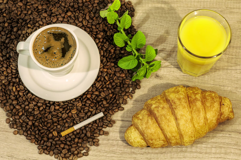 木桌上的一杯新鲜咖啡咖啡豆牛角面包果汁雪茄和薄荷茶花