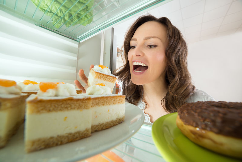 饥饿的年轻女子在家吃冰箱里的蛋糕片